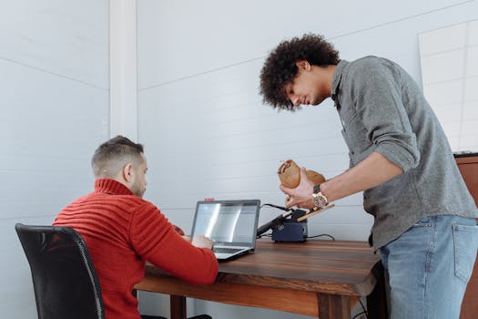 Two adults engaged in collaborative work using a laptop in a modern office.