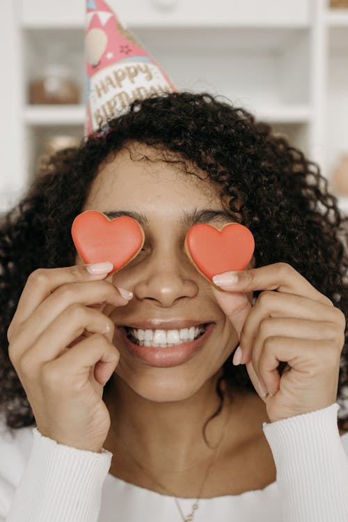 Woman Smiling while She Holds a Heart Shaped Cookie in Front of Her Eyes