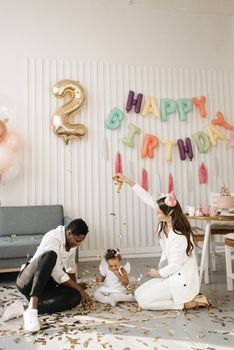 A joyful indoor family celebration with balloons and confetti, marking a child's second birthday.