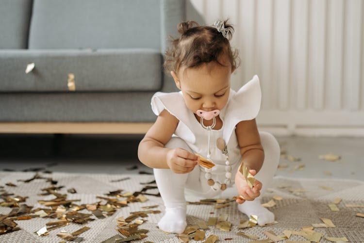 Child In White Dress Enjoy Picking Up Confetti On Her Birthday