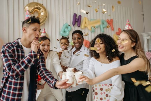 A vibrant group of friends celebrating a birthday indoors with cheers and confetti.