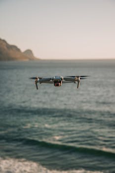 Aerial shot of a drone flying over the ocean with Cape Town's coastal landscape in the background.