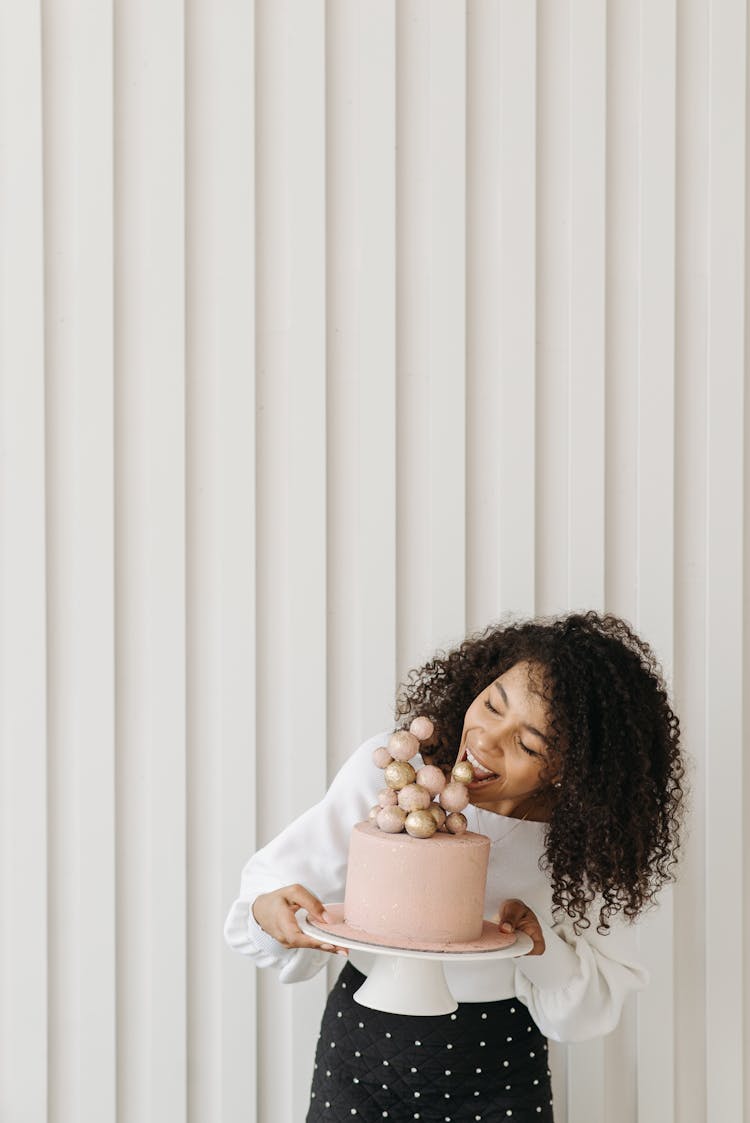 Woman In White Long Sleeve Shirt Holding A Cake And Trying To Bite It