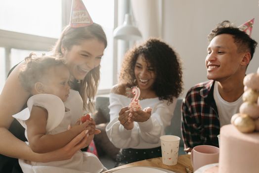 A happy family celebrates a child's birthday with a cake and decorations indoors.