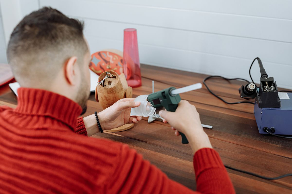 Crafter using a hot glue gun at a wooden workspace to make a rustic sign