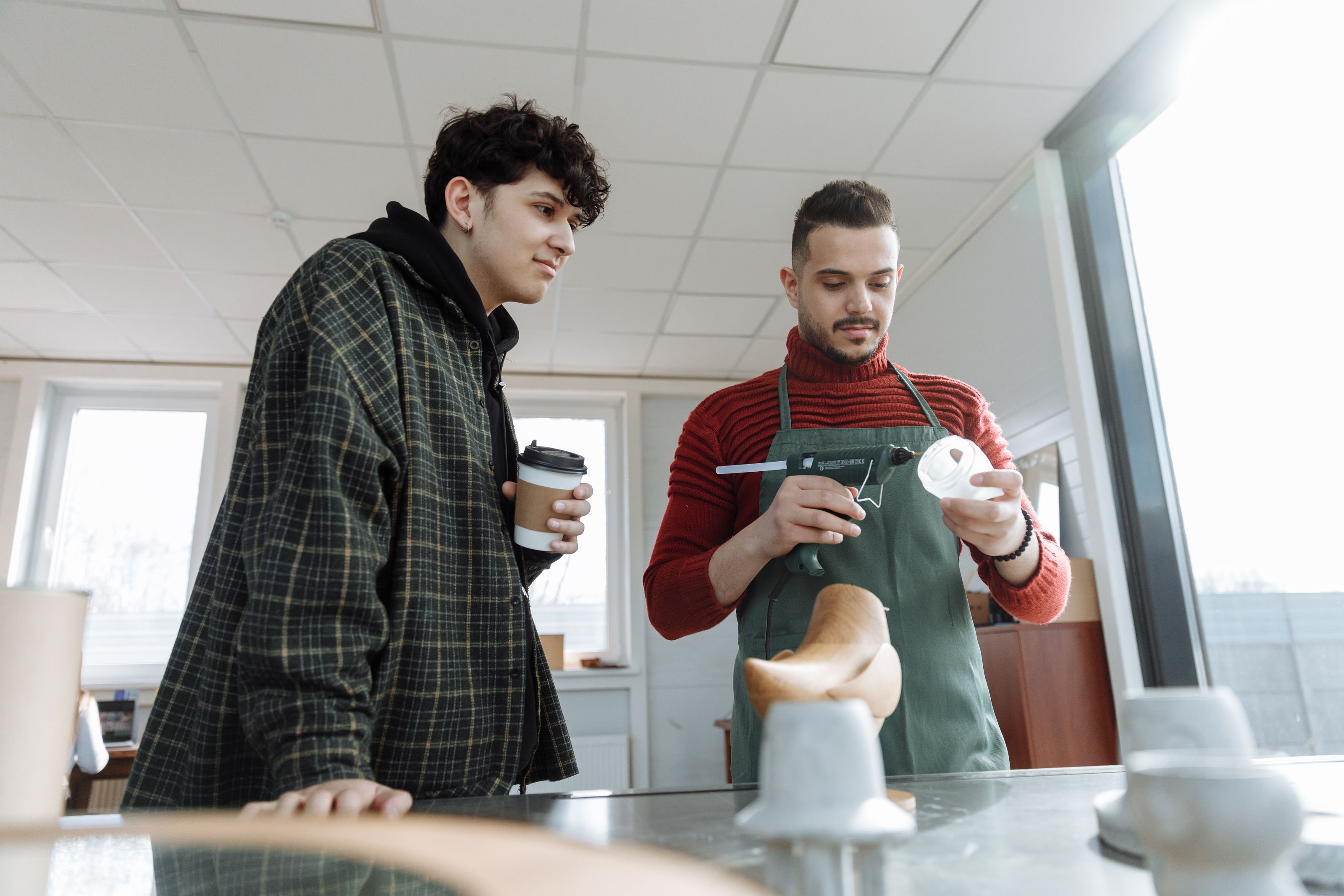 Two young men in a crafting workshop working with a glue gun, focusing on craftsmanship indoors.