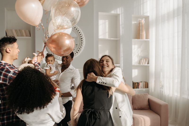 A diverse group enjoying a lively birthday celebration with balloons, hugs, and smiles.