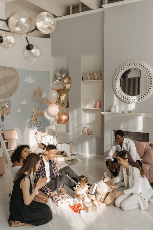 Free Happy People Sitting on the Floor while Looking at the Baby Opening the Gifts Stock Photo
