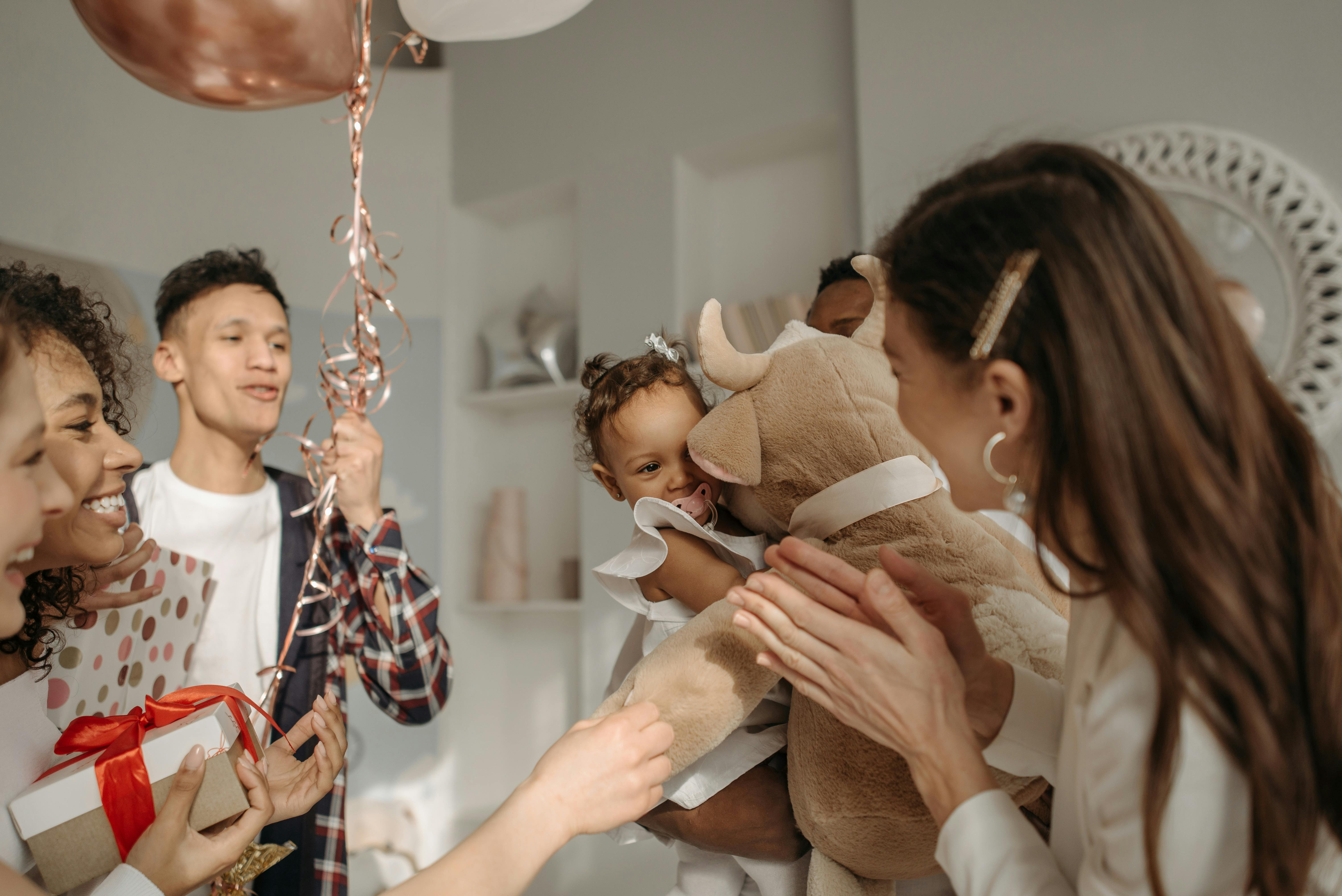 A cheerful family gathering indoors with balloons, gifts, and a smiling baby.
