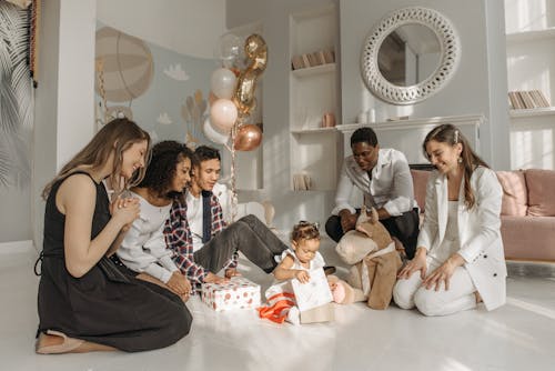 People Sitting on the Floor and Watching Baby Girl Opening Gift Box