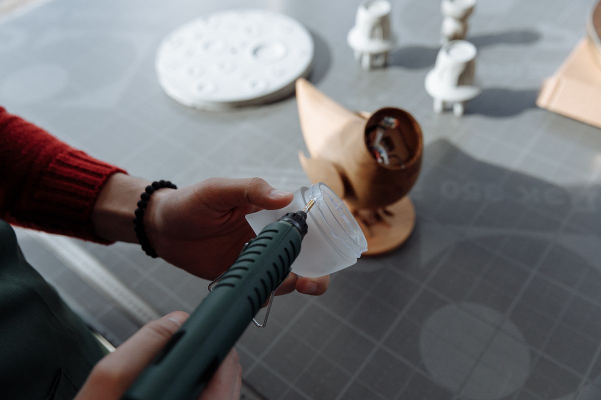 Hands using a glue gun to craft a wooden figurine in a workshop setting