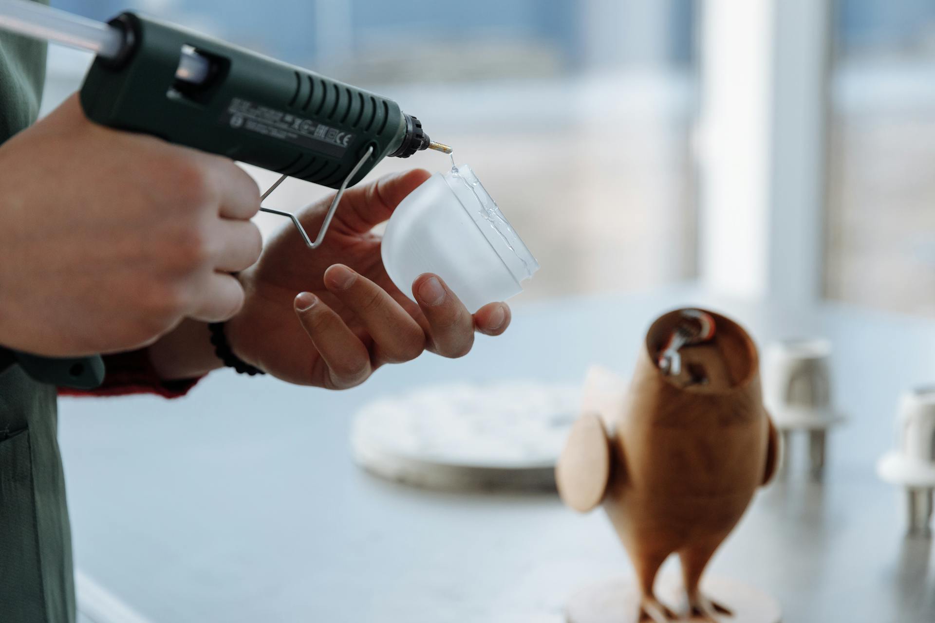 Close-up of hands using a glue gun to craft a wooden figurine in a workshop setting.