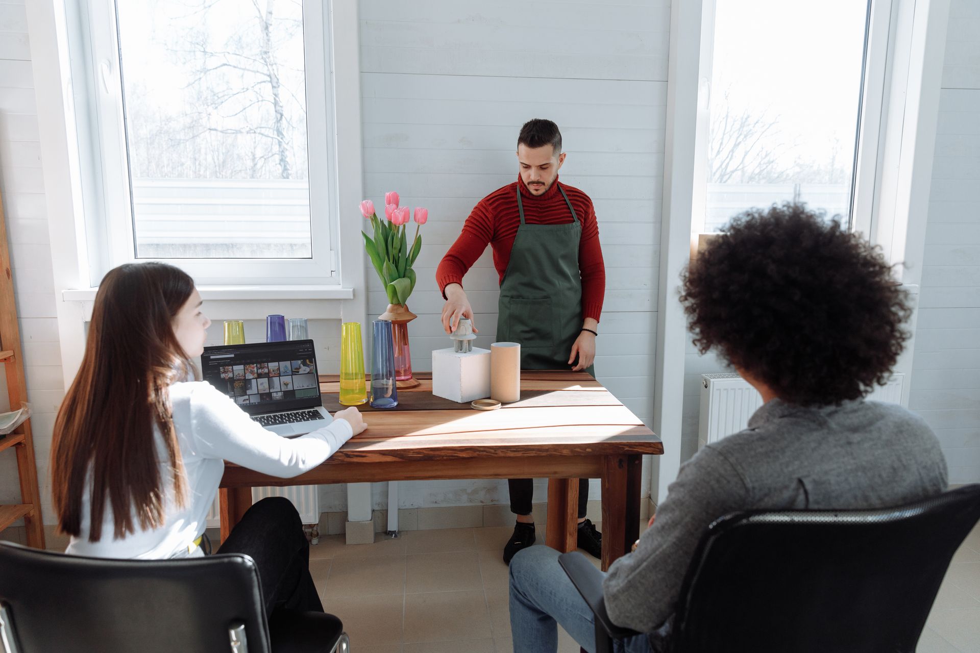 Two people watch a barista demonstrate coffee brewing at a table.