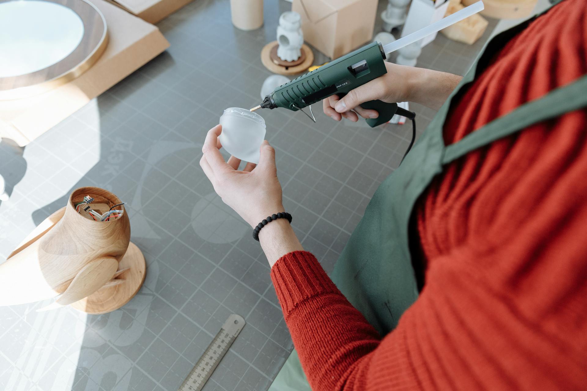 Handmade figurine assembly using a glue gun in a well-lit workshop environment.