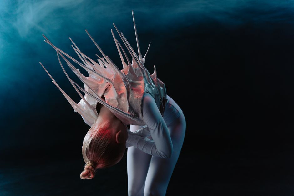 Close-up of a person in a futuristic costume with spikes, bent over against a dark background.