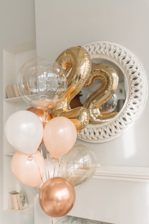 Free White and Gold Balloons Beside a Mirror Hanging on White Wall Stock Photo