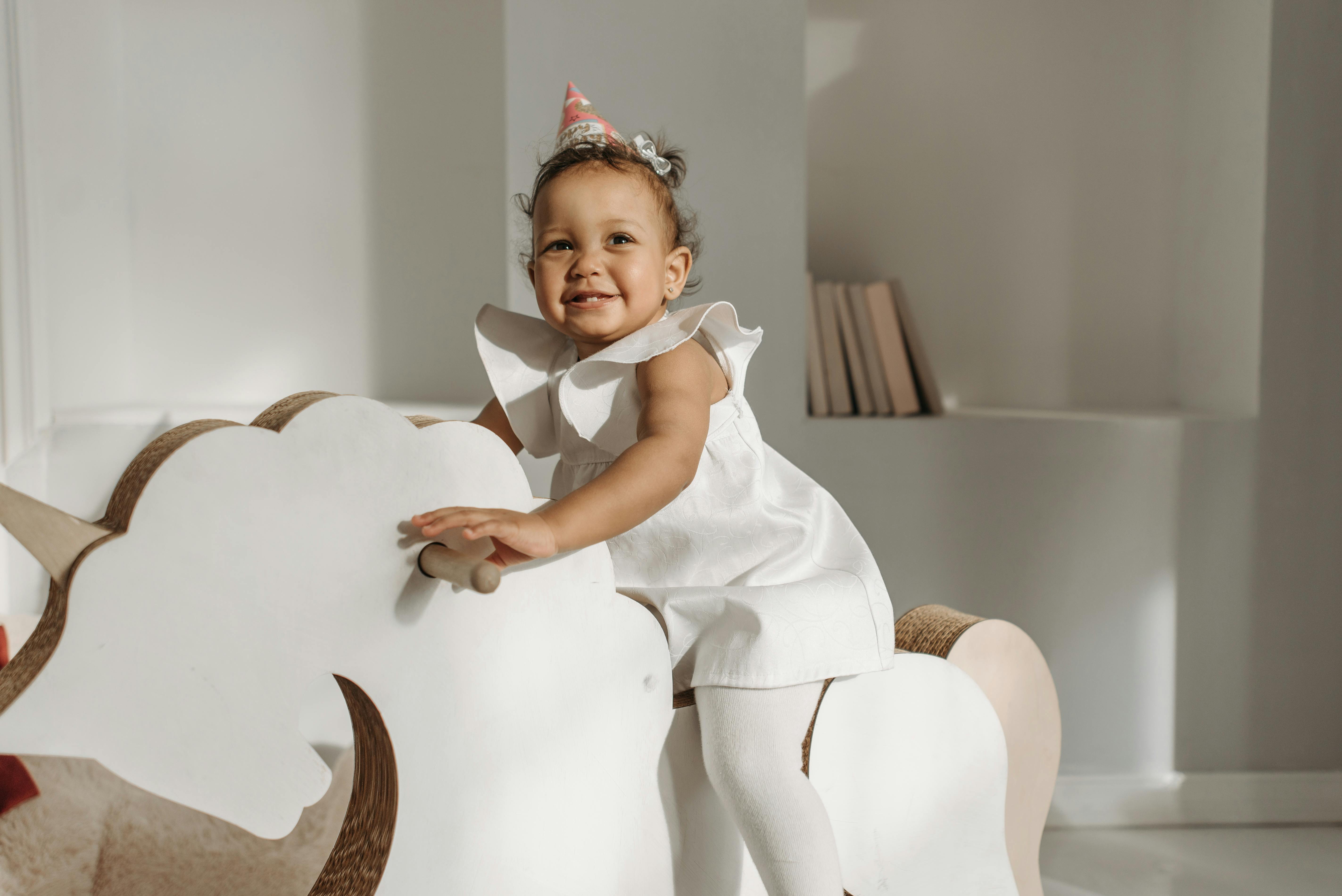 baby girl in white dress sitting on rocking horse
