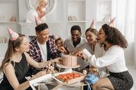 A Group of People with Party Hats Sitting at a Table with a Birthday Cake