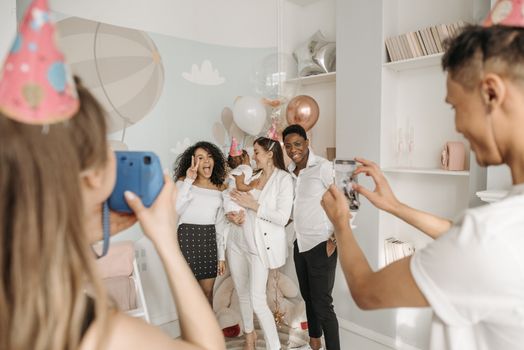 Group of friends celebrating a birthday indoors with balloons and party hats, captured in a joyful moment.