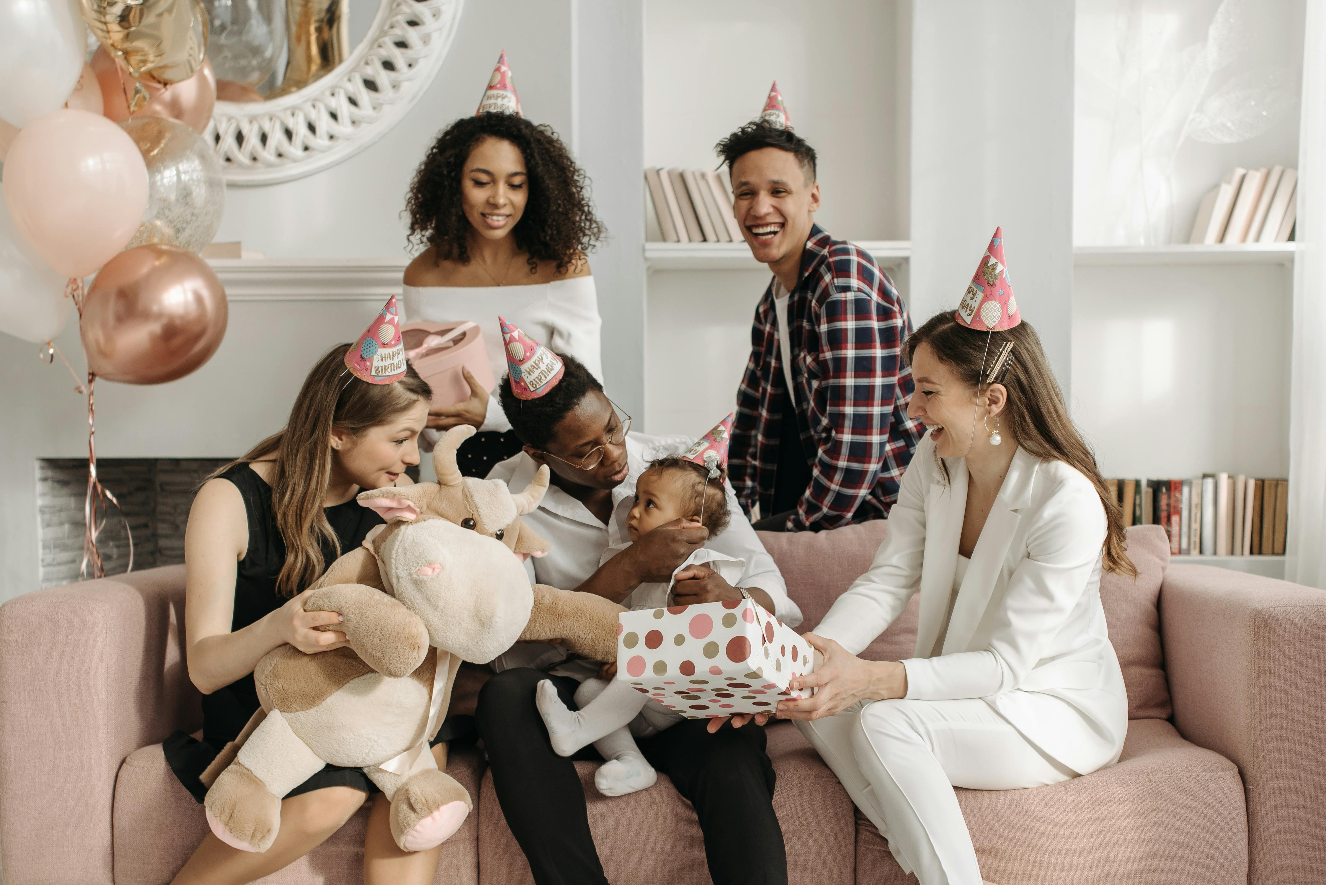 baby girl sitting on the man s knees while woman in white suit sitting on couch and holding polka dotted gift box