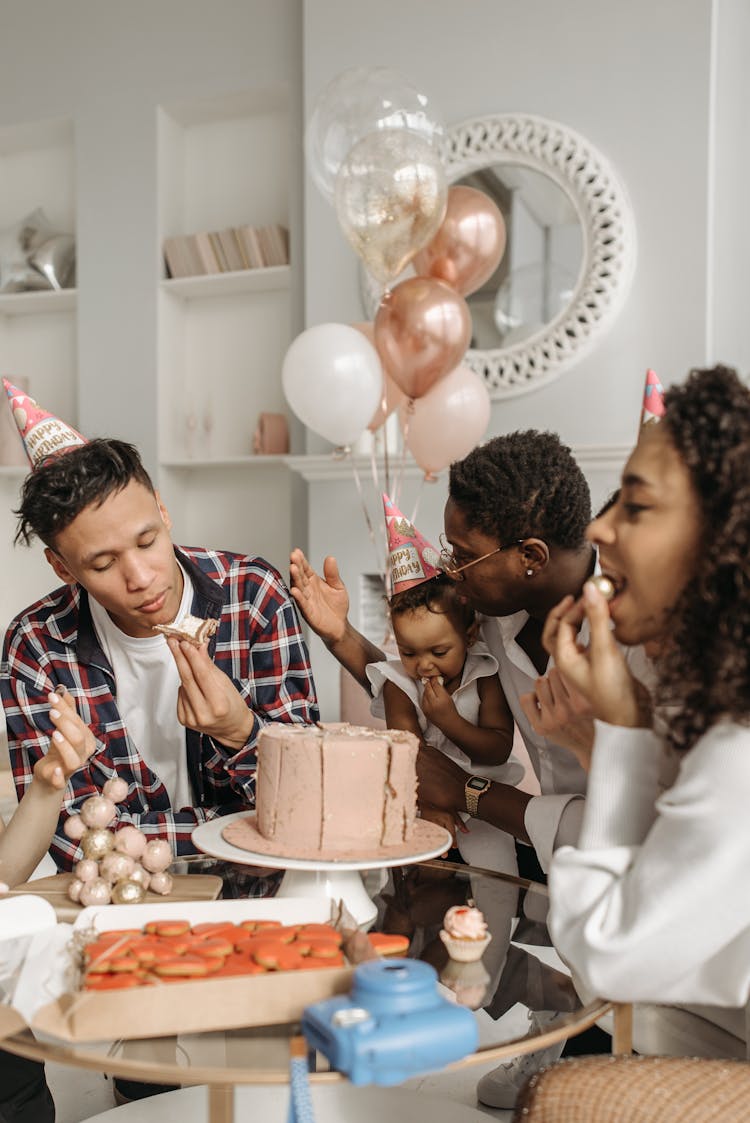 A Family With Birthday Hats Eating Together At The Table