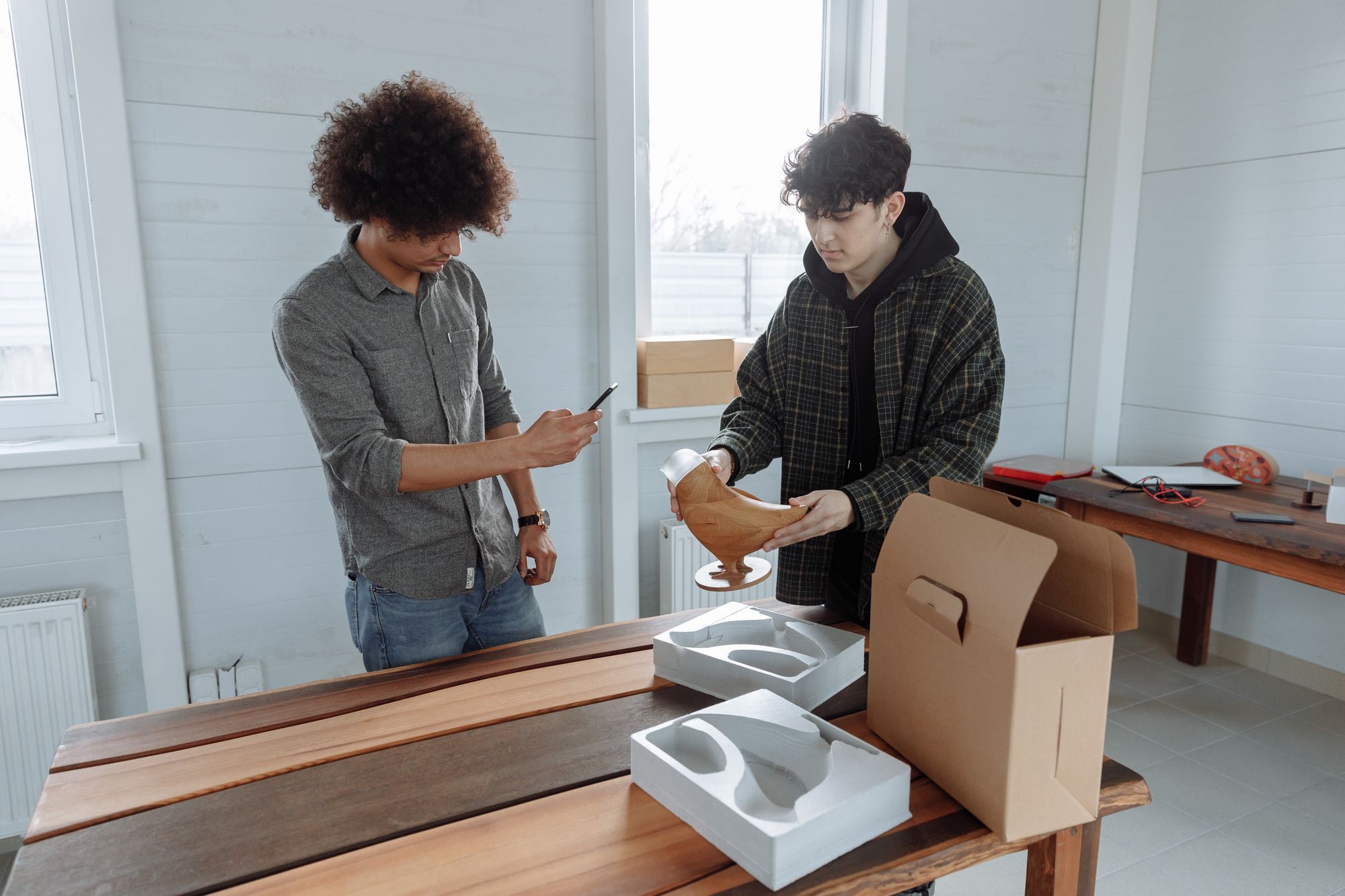 Two men working together in a workshop to package a handcrafted wooden item, with a focus on craftsmanship and teamwork.