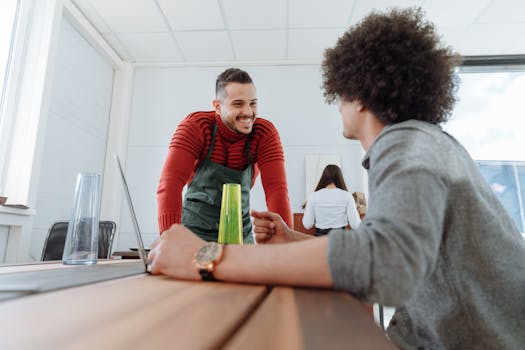 Two professionals engaged in a casual conversation in a modern office setting with natural light.