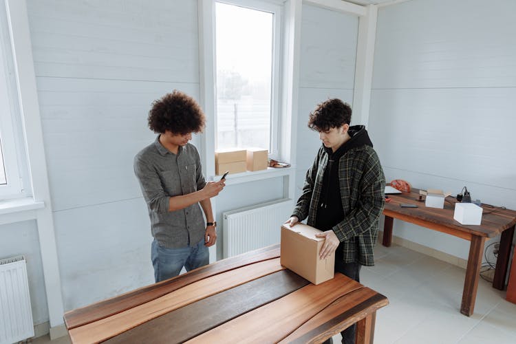 Man With Curly Hair Recording Man In Plaid Jacket Unpacking The Box