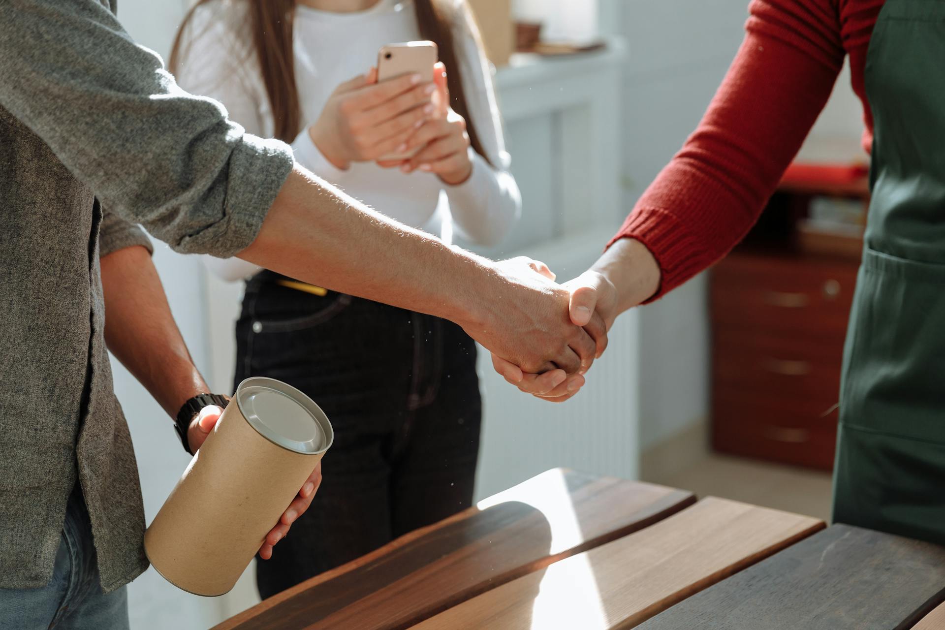 Three people meeting with a handshake in a bright office setting, promoting teamwork and collaboration.