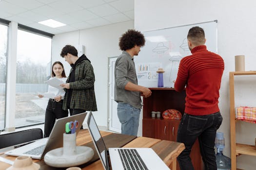 Young professionals brainstorming at a modern office with laptops and a whiteboard, showcasing teamwork and innovation.