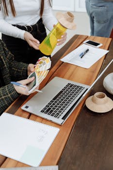 Designers working with color swatches, a laptop, and creative tools at a wooden table.