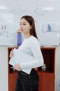 A thoughtful young woman holds a notebook in a creative design studio setting.