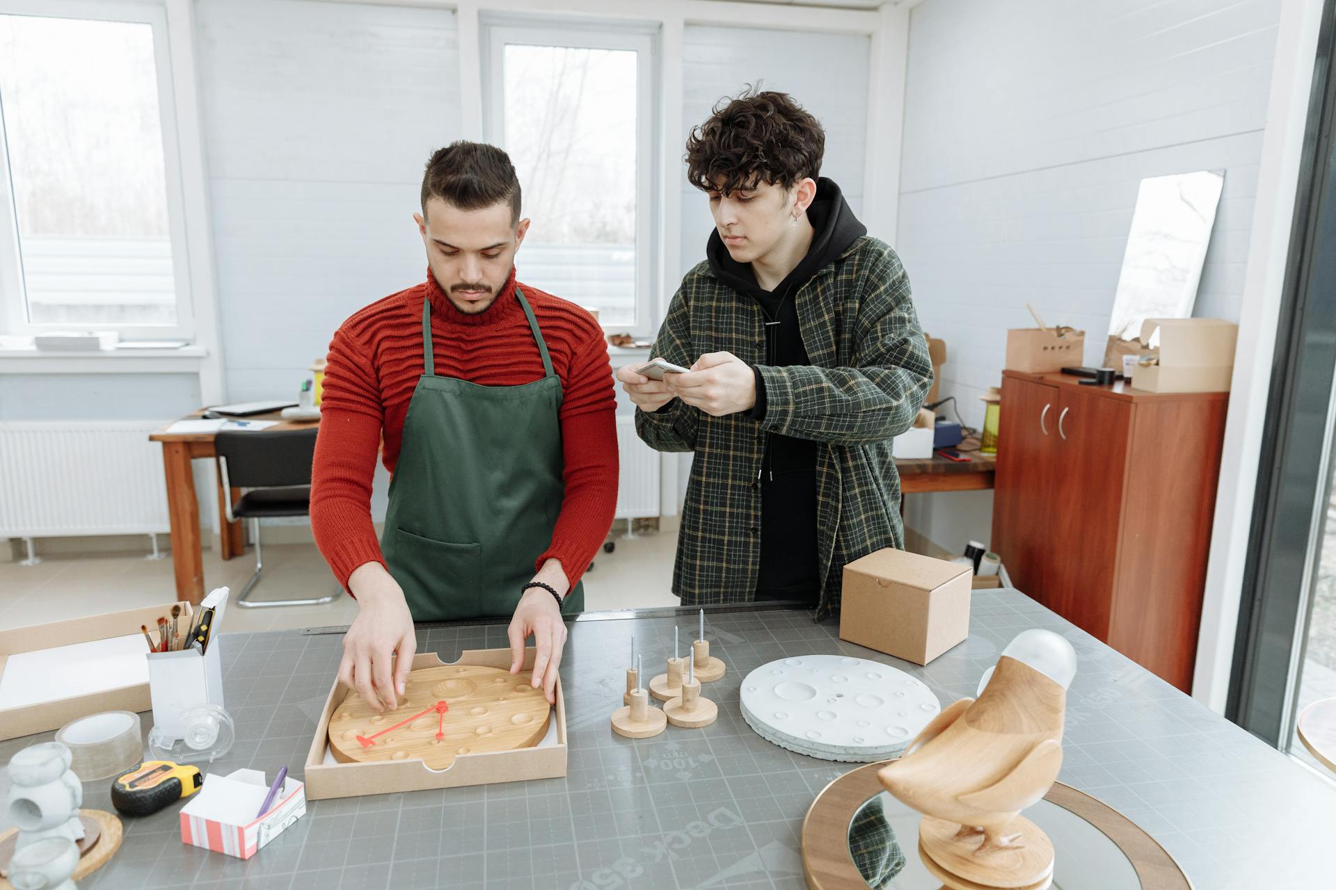 Man in Plaid Jacket Taking Photo of Man in Red Sweater Packing Wooden Clock