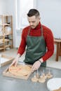 Man in Red Sweater and Green Apron Holding Wooden Clock