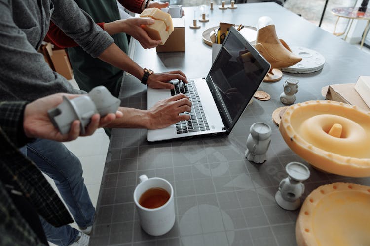 People Standing Beside Man Using Laptop On Gray Table With Silicon Forms