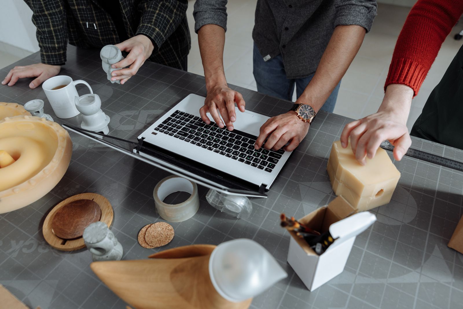 A studio team working over prototypes and a laptop on a cutting mat — photo by Thirdman on Pexels