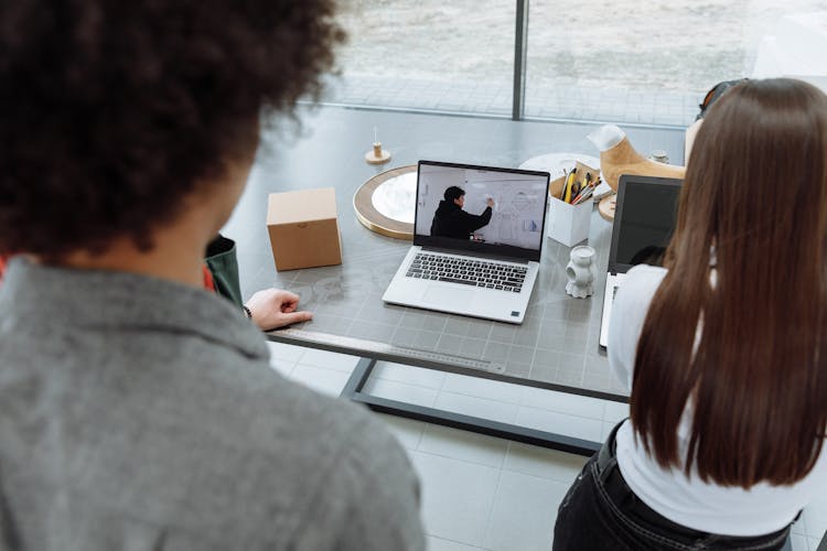 People Standing In Front Of A Laptop With A Person Drawing On A White Board