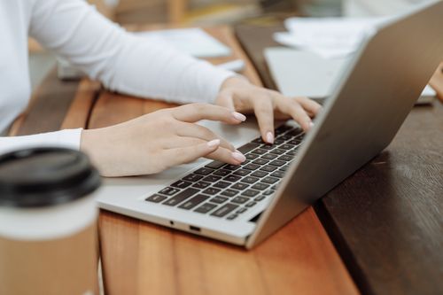 Free Close-up of a woman's hands typing on a laptop next to a coffee cup in a casual setting. Stock Photo