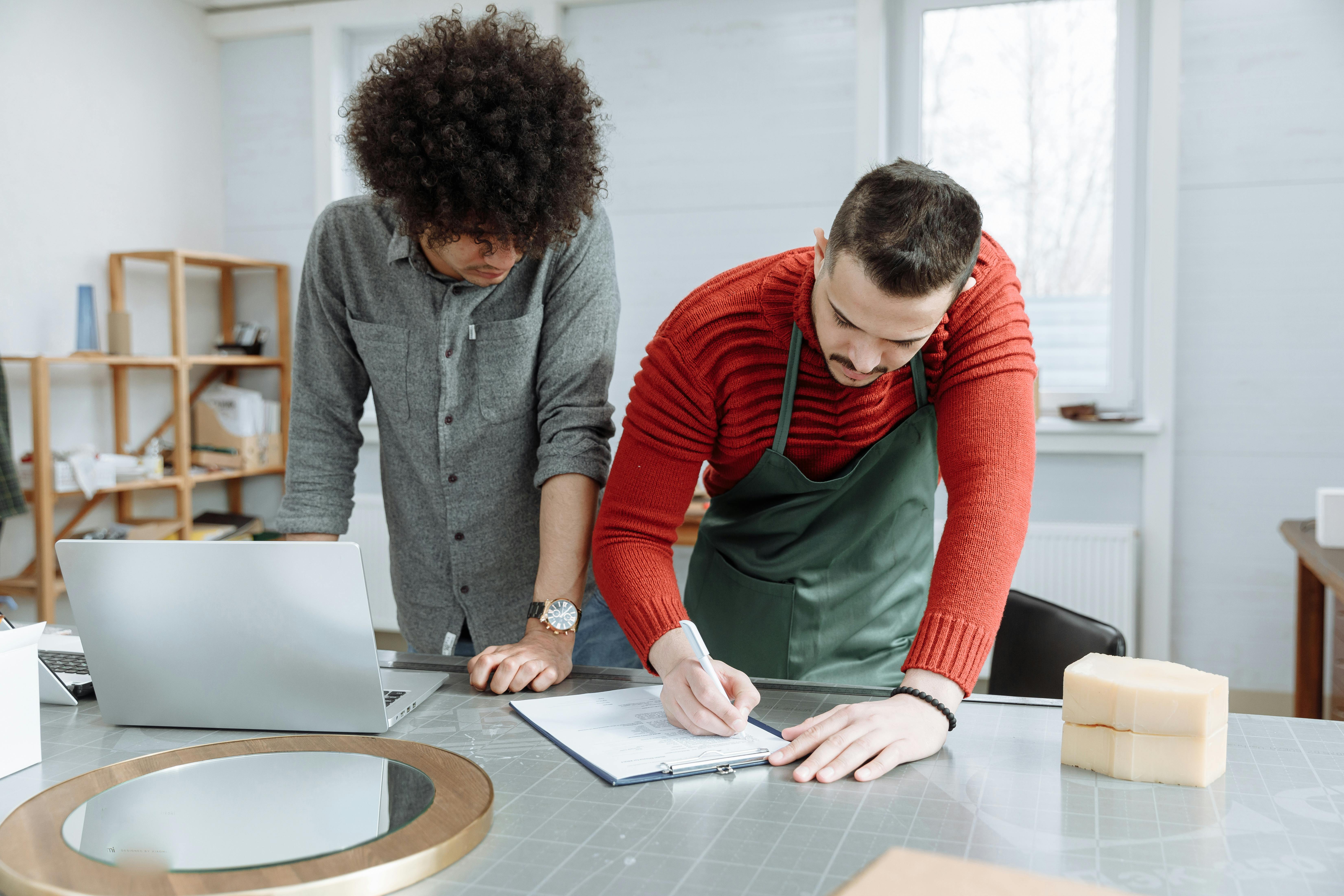 a man in red sweater writing on paper beside a man