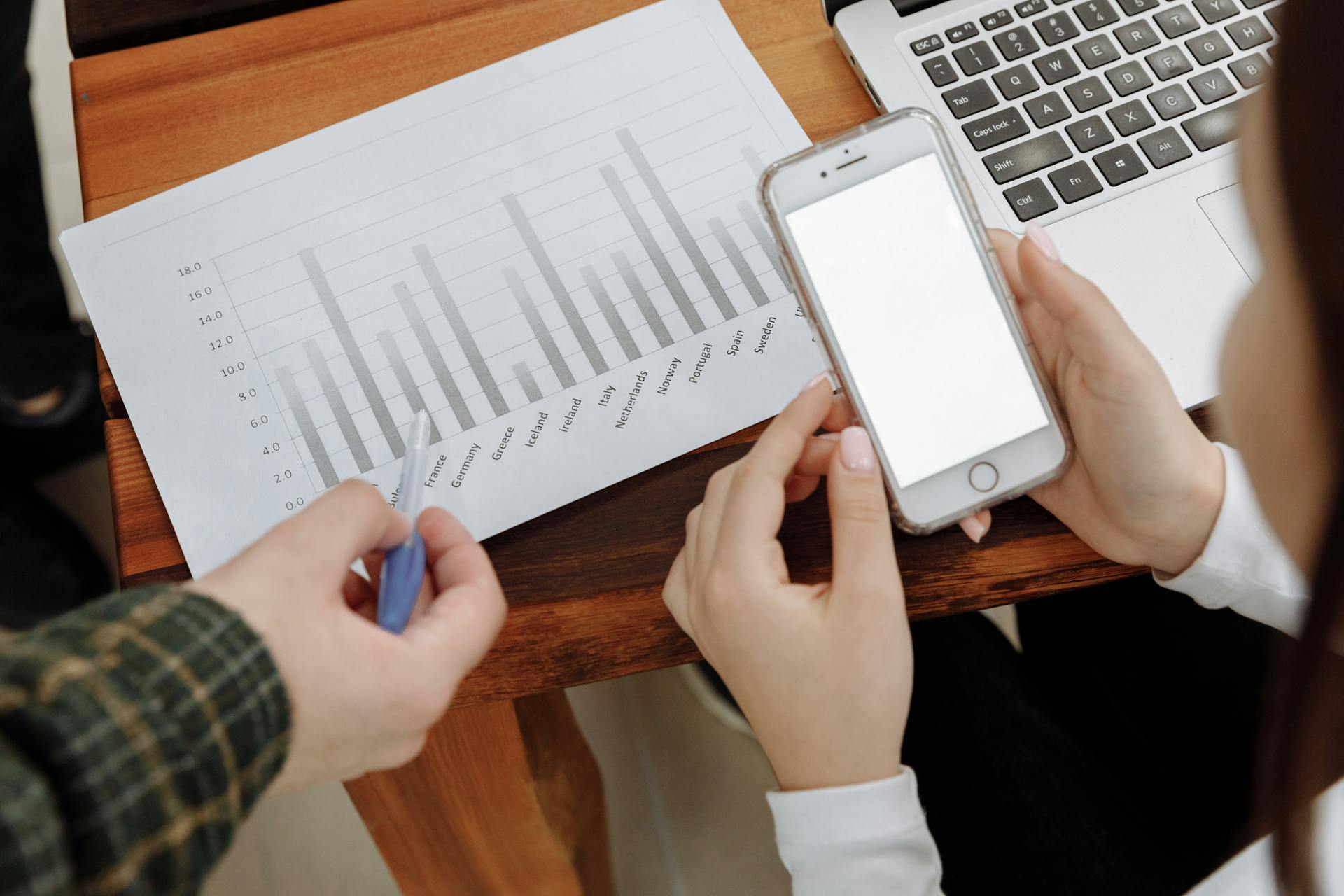 A business professional reviews data on a smartphone and printed chart in an office setting.