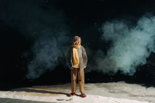 A woman wearing a yellow scarf stands amid dramatic smoke on a dark backdrop, creating a mysterious atmosphere.