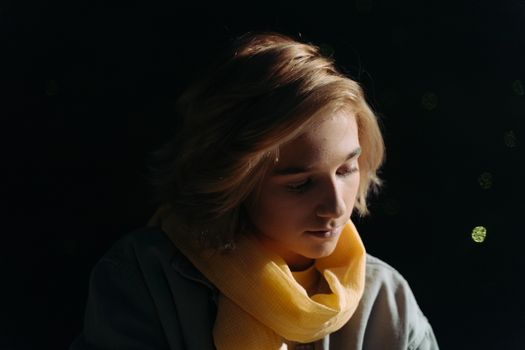 A serene portrait of a young adult wearing a yellow scarf, bathed in gentle light.
