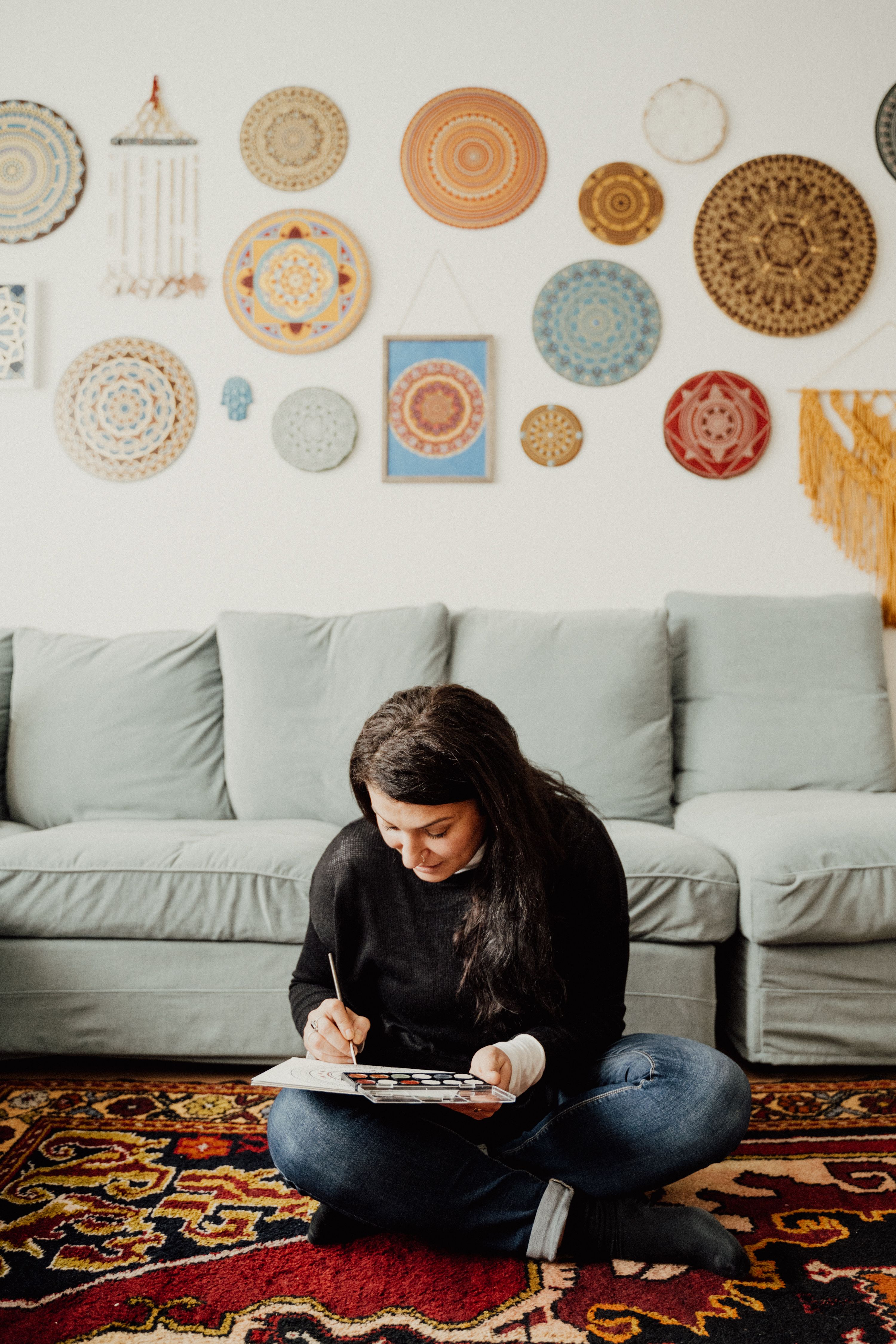 Woman painting in a cozy living room with mandala wall art, showcasing creative expression.