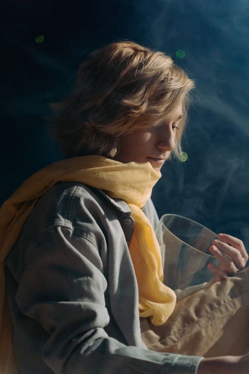 Free Young person in a soft lighting with a yellow scarf enjoying a warm beverage. Stock Photo