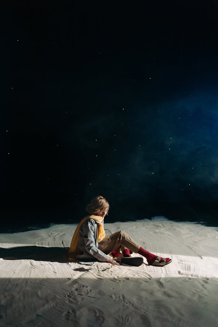 A Boy Wearing A Yellow Scarf Sitting On Sand