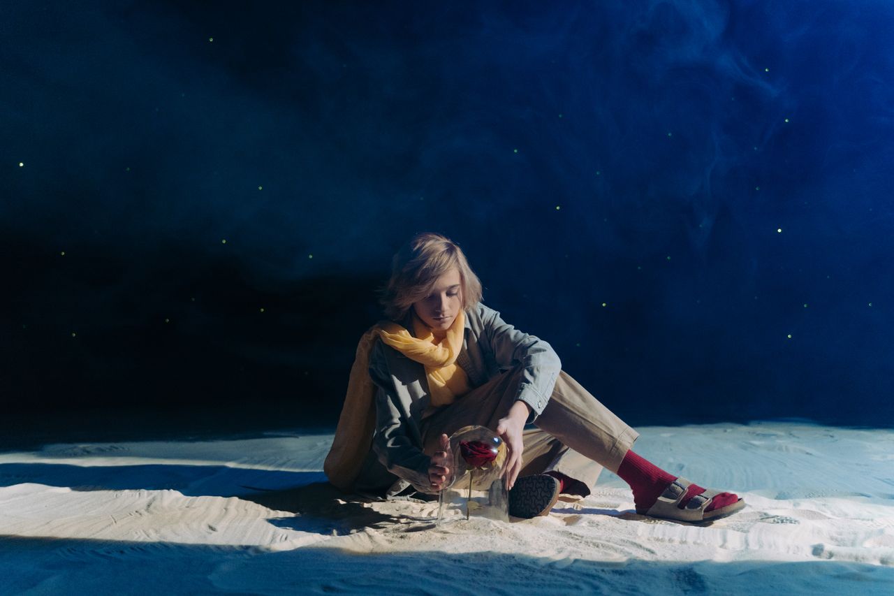 a young person in cosplay sits in a dreamy starry setting with sand an