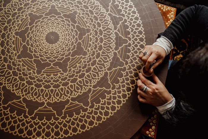 Intricate mandala being hand-drawn onto canvas in gold line — photo by Alesia Kozik on Pexels