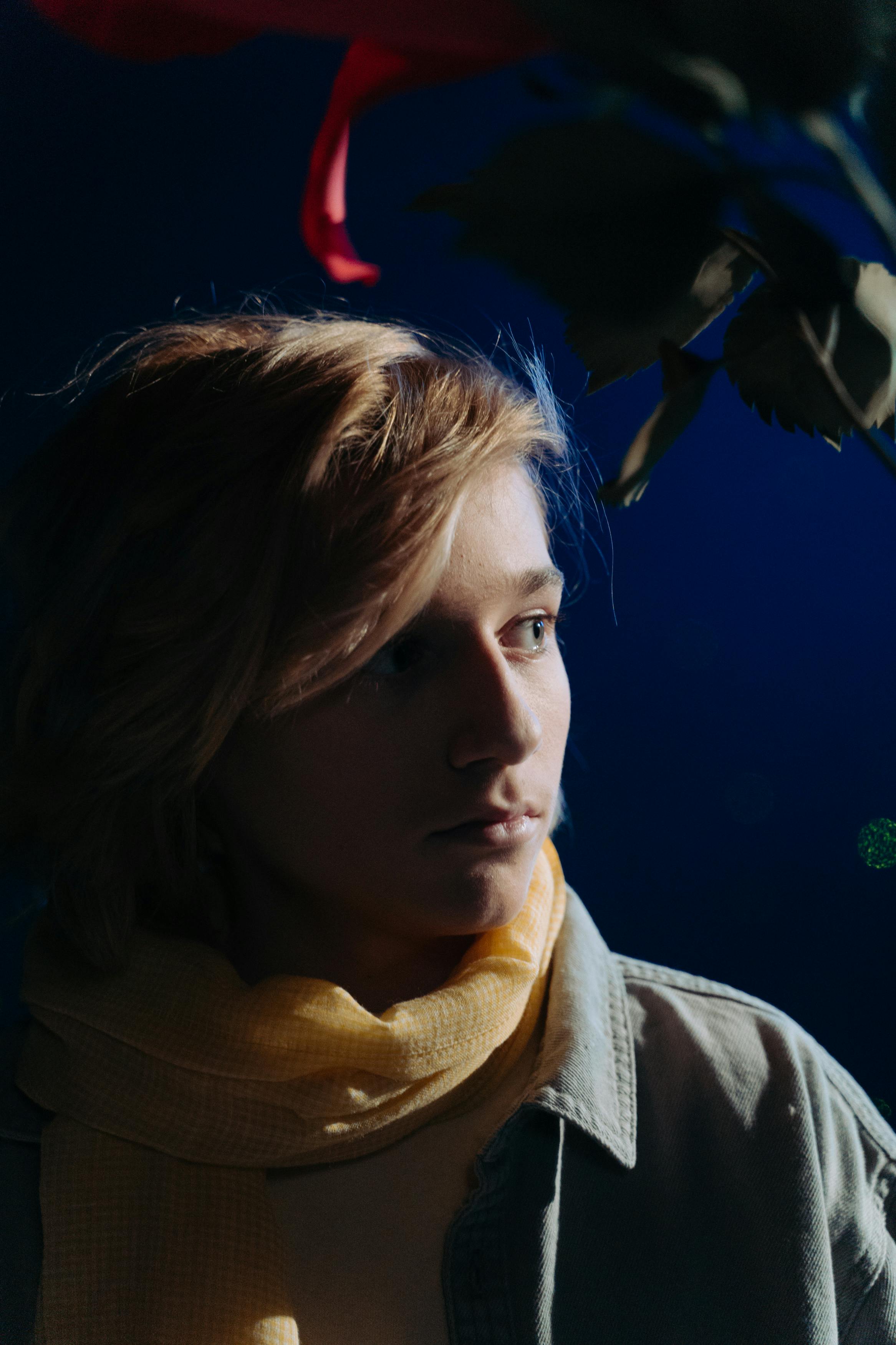 Moody portrait of a young person with a yellow scarf under dramatic lighting.