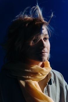 Stylish portrait of a young man wearing a scarf against a dark blue background.