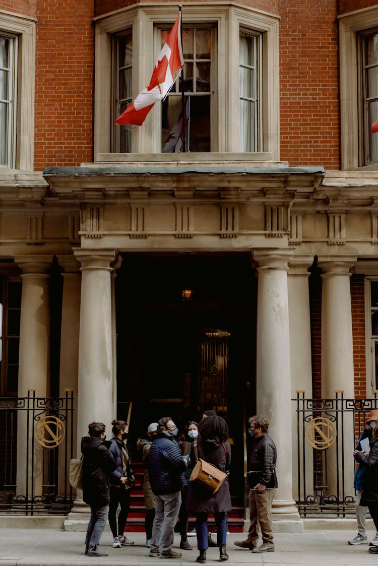 People In Face Masks Near Building With Flag